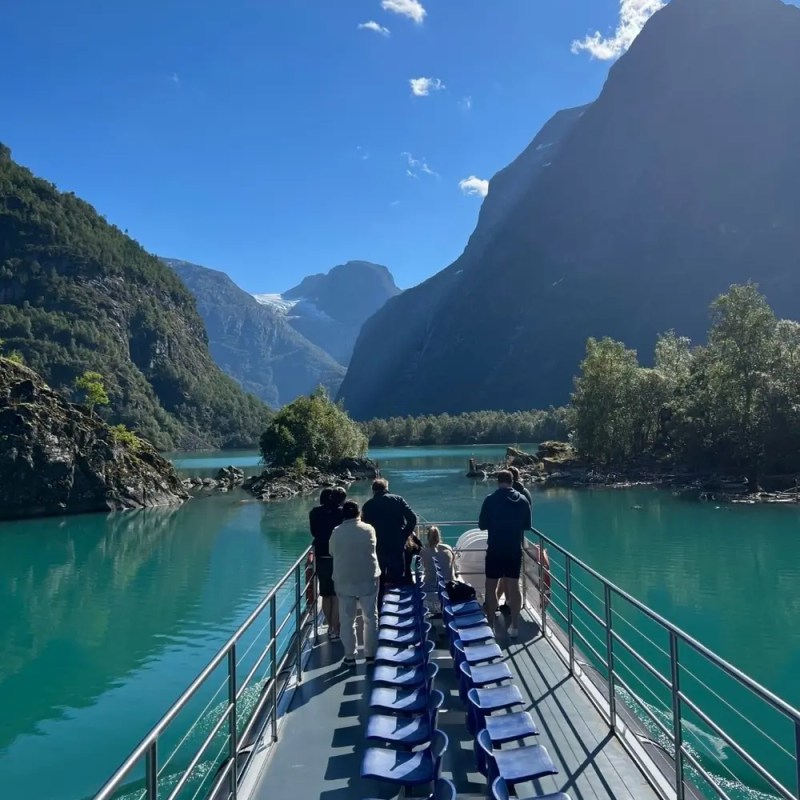 Tourists on a boat in a turquoise fjord, surrounded by mountains.