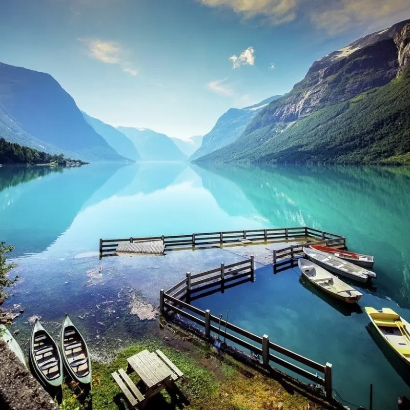 Calm turquoise lake surrounded by mountains, with boats at a wooden pier.