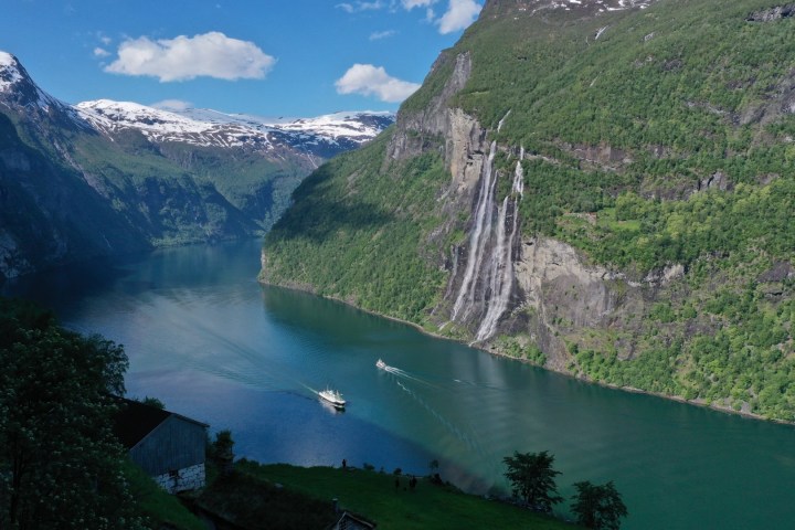 Scenic fjord with a waterfall and boats in clear water surrounded by mountains.